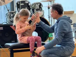 Ukulele-Unterricht: Lehrer gibt einem Mädchen in einem Musikraum eine High-Five.