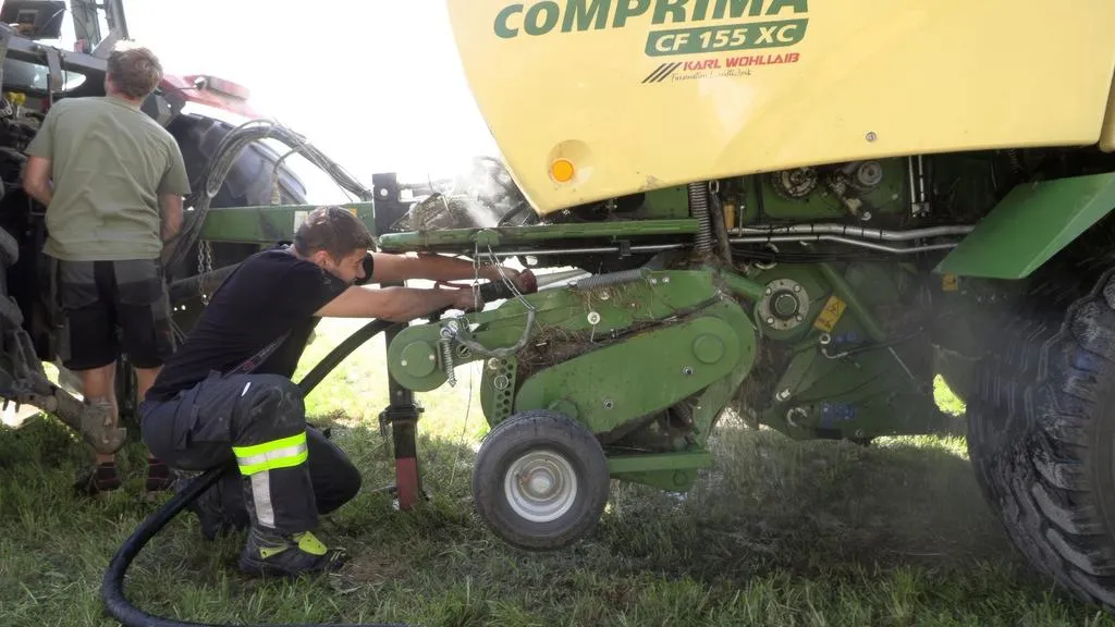 Landwirtschaftliche Techniker reparieren Presswickler der Marke Claas in einem Feld in Österreich.
