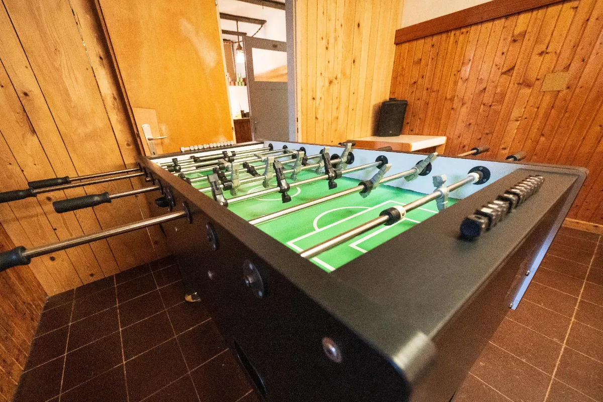 Tischfußball mit grünen Spielfeld und schwarzen Figuren in einem Raum mit Holzwand