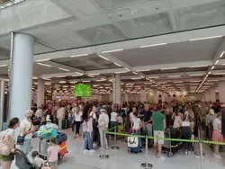Flughafen: Menschen mit Gepäck warten in einer langen Schlange am Check-in-Schalter.