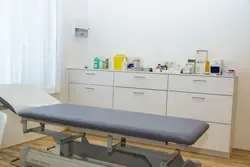 Arztliege und medizinische Geräte in einem Behandlungsraum einer Praxis in Österreich.