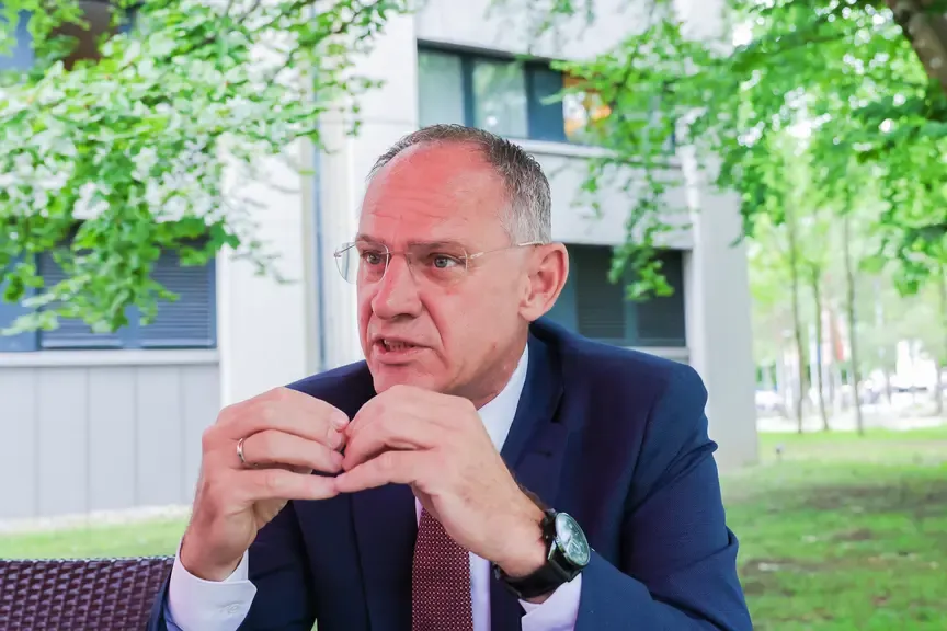 Karl Nehammer, Bundeskanzler, spricht mit den Händen vor einem Gebäude mit Bäumen.