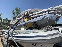 Frau mit gelbem Pullover und weißer Kappe sichert Schlauchboot mit Nummer 1557 ST auf einem Anhänger.