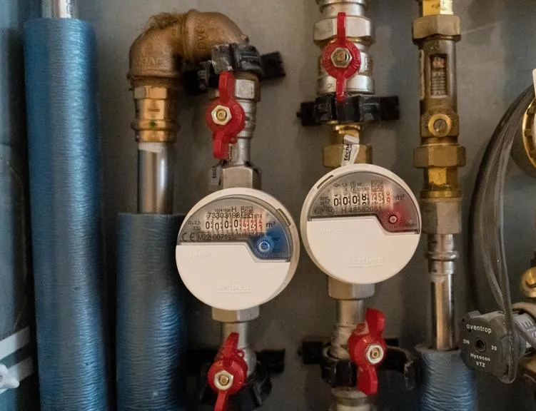 Wasserzähler mit roten Absperrhähnen und gedämmten Rohren in einem Heizungsraum