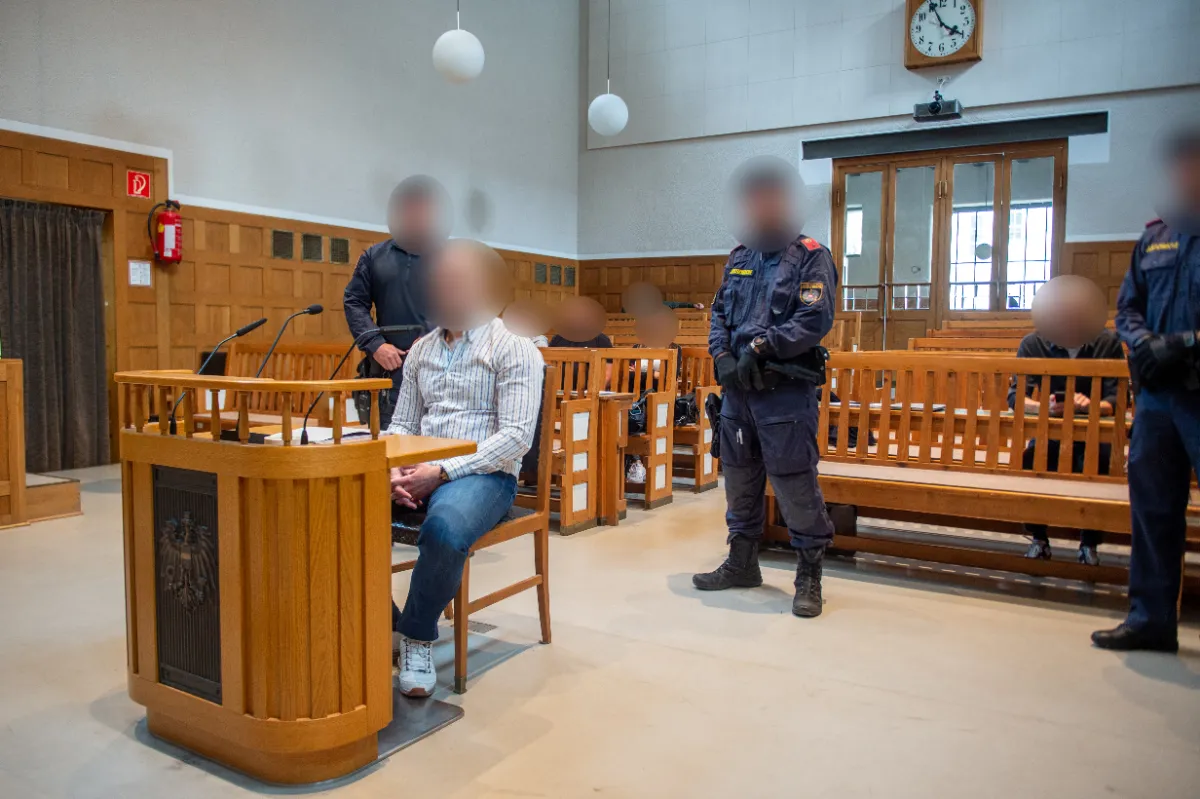 Angeklagter sitzt im Gerichtssaal, Polizisten stehen Wache im Justizpalast Wien.