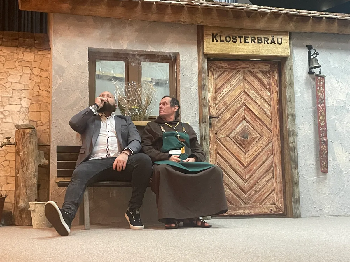 Männer vor Klosterbräu-Tafel rauchend und sitzend.