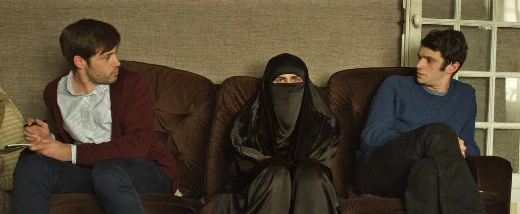 Frau mit Nikab und zwei Männer sitzen auf einem braunen Sofa in einem Raum.