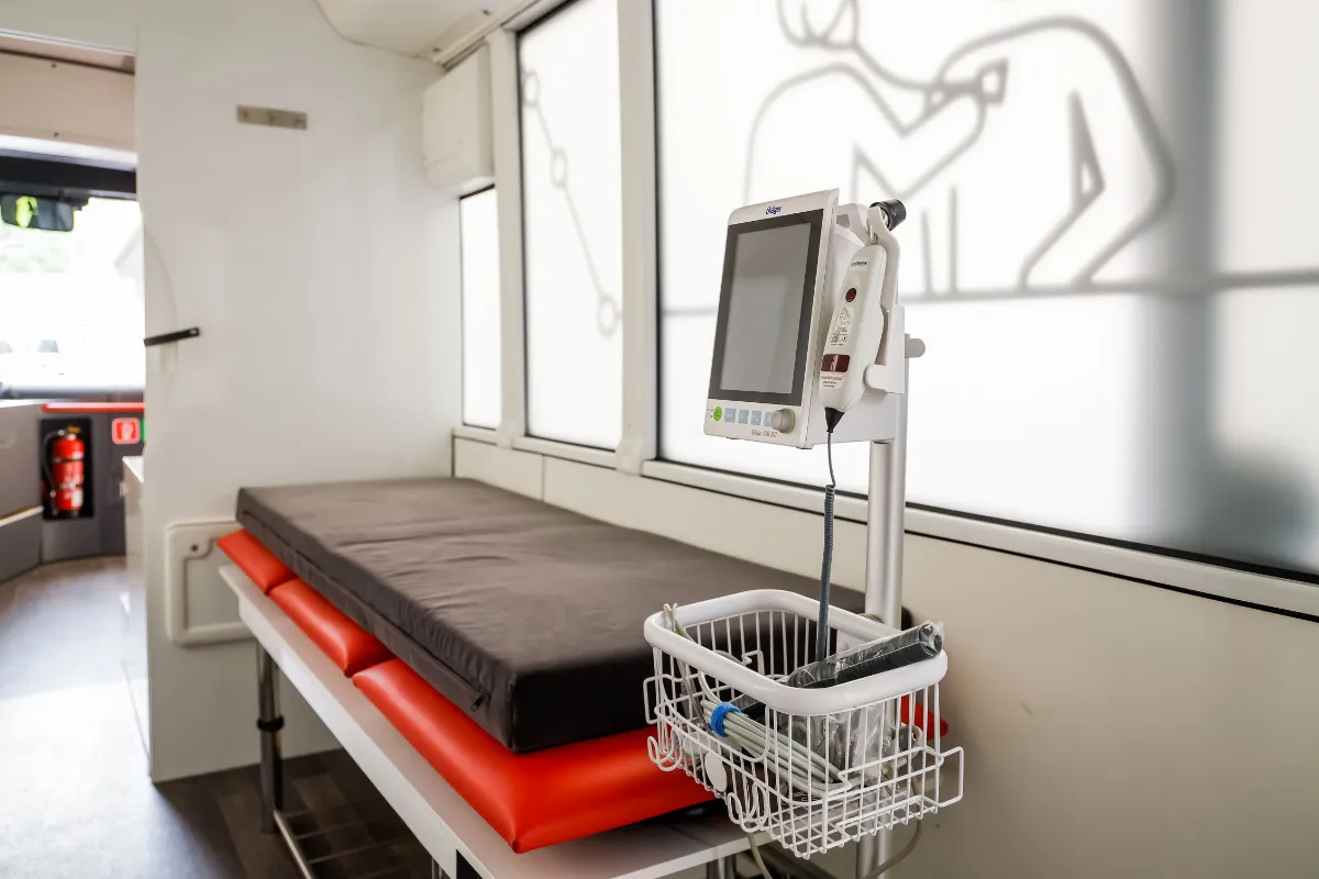 Untersuchungsliege mit medizinischem Monitor und Zubehör in einem mobilen Behandlungsraum.