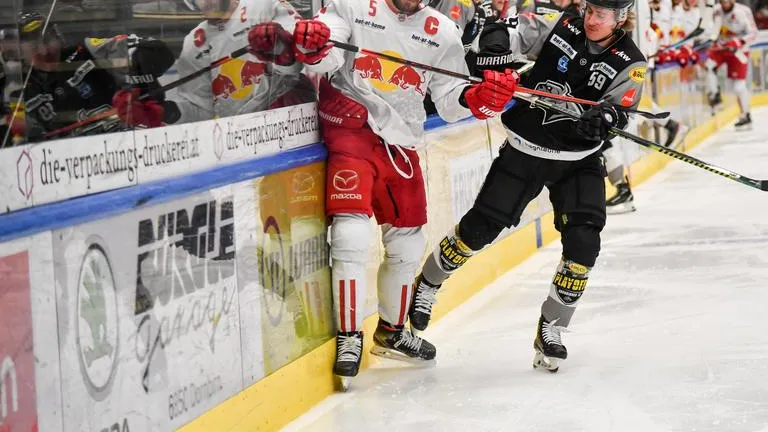 Eishockey-Spieler im Zweikampf um den Puck an der Bande in der Eisarena.