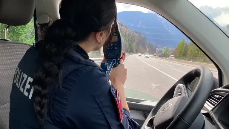 Polizistin misst mit Radarmessgerät Geschwindigkeit auf der Autobahn in bergiger Landschaft
