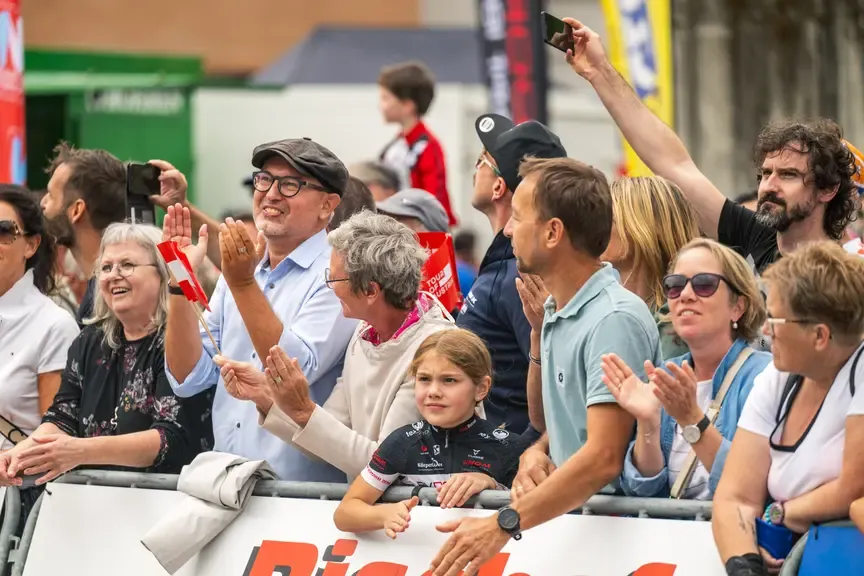 Zuschauer beim Radrennen Tour of Austria klatschen und halten Fahnen.