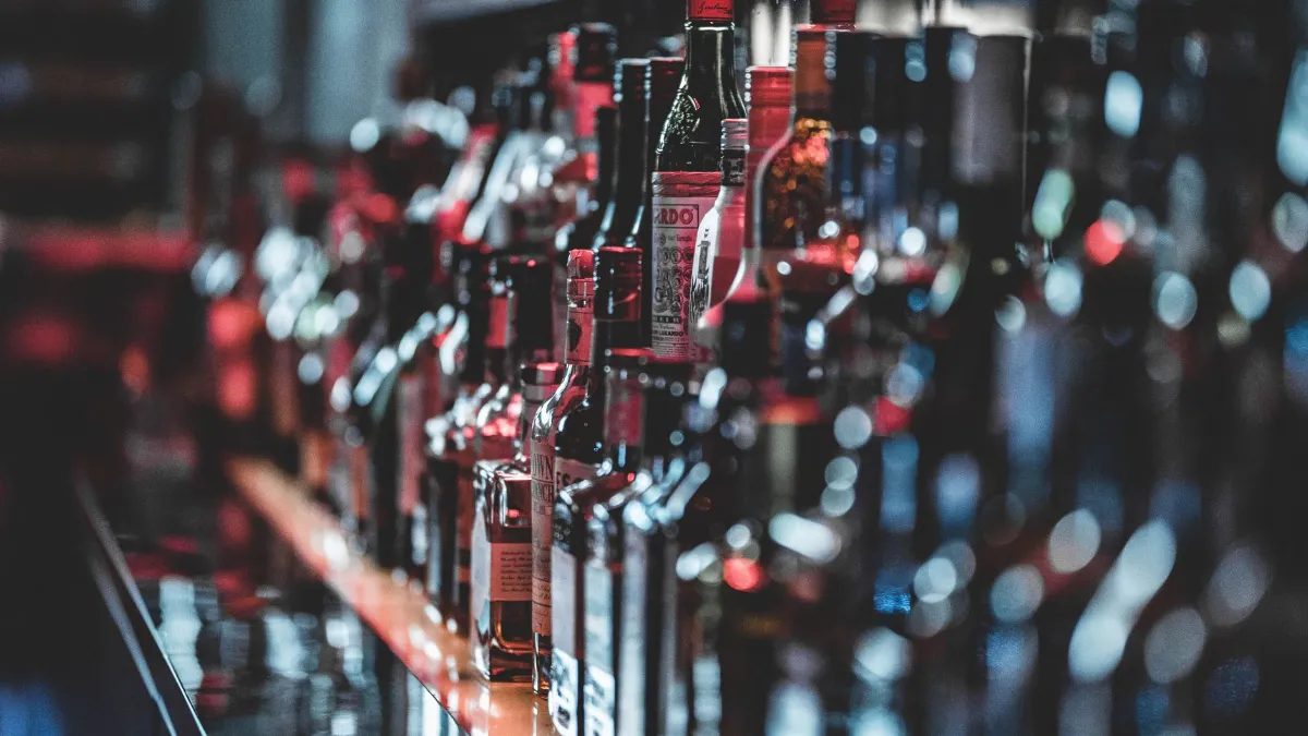 Flaschen mit Alkohol stehen in einer Bar in einer Reihe, rote und blaue Lichter spiegeln sich.