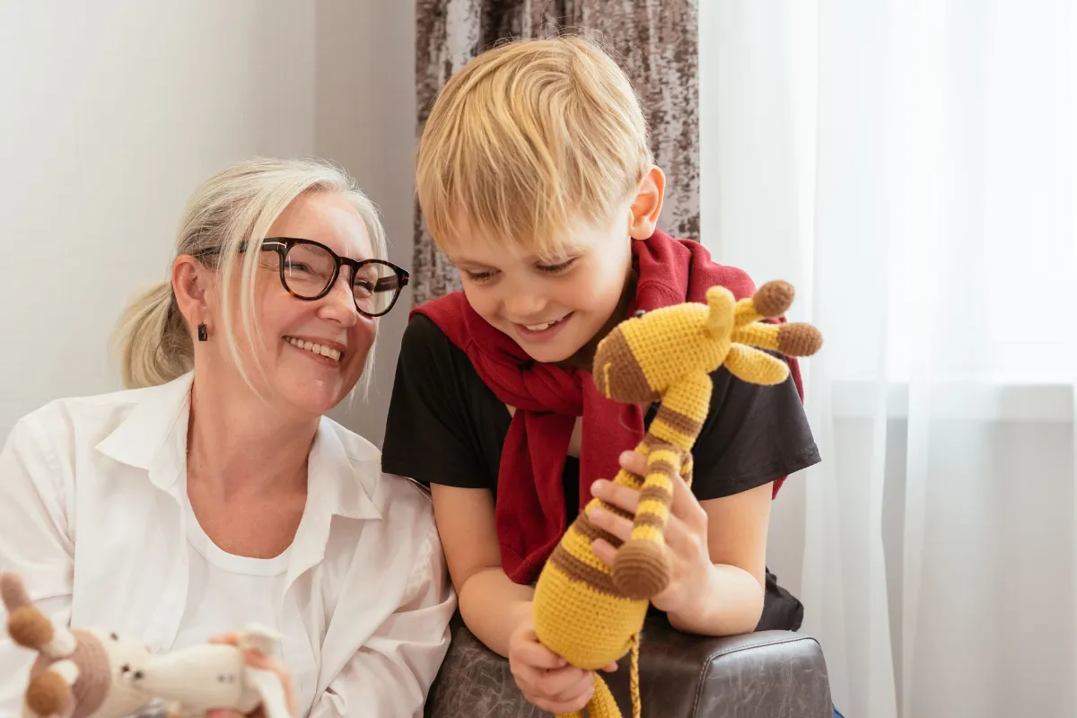 Frau mit Brille und Großkind mit gehäkelter Giraffe im Arm lächeln sich an.
