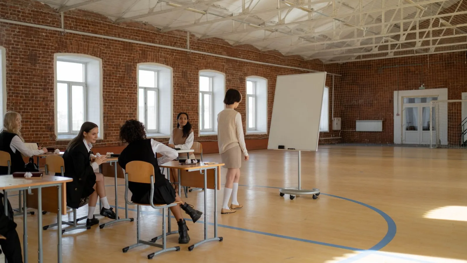 Schülerinnen in einem Turnsaal mit Tafel und Sitzreihen