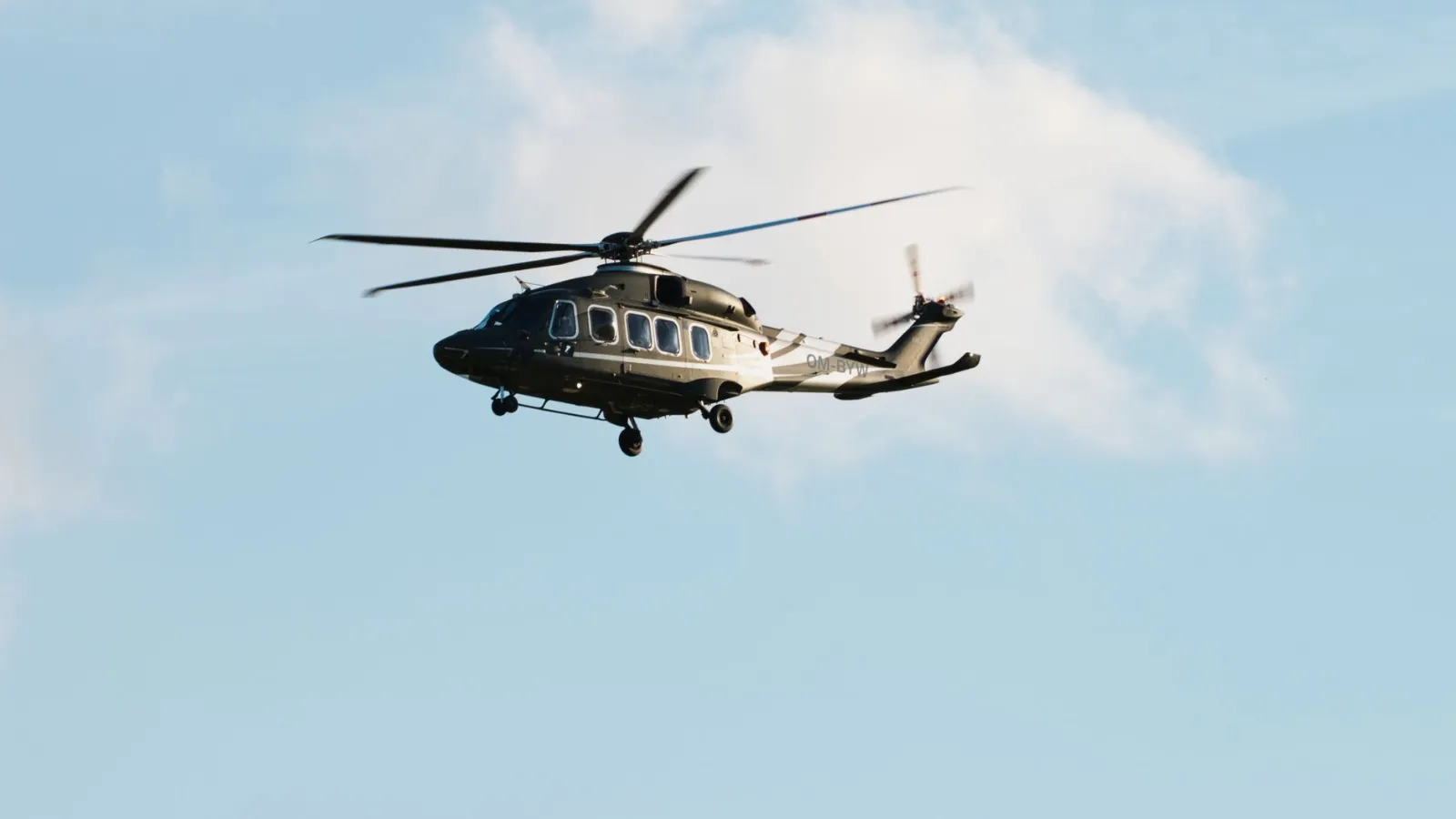 Helikopter fliegt vor blauem Himmel mit Wolken, Kennzeichen OM-BYW