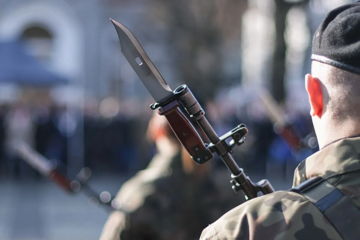 Bajonett an einem Gewehr, Soldat mit Tarnanzug und schwarzer Kappe im Hintergrund