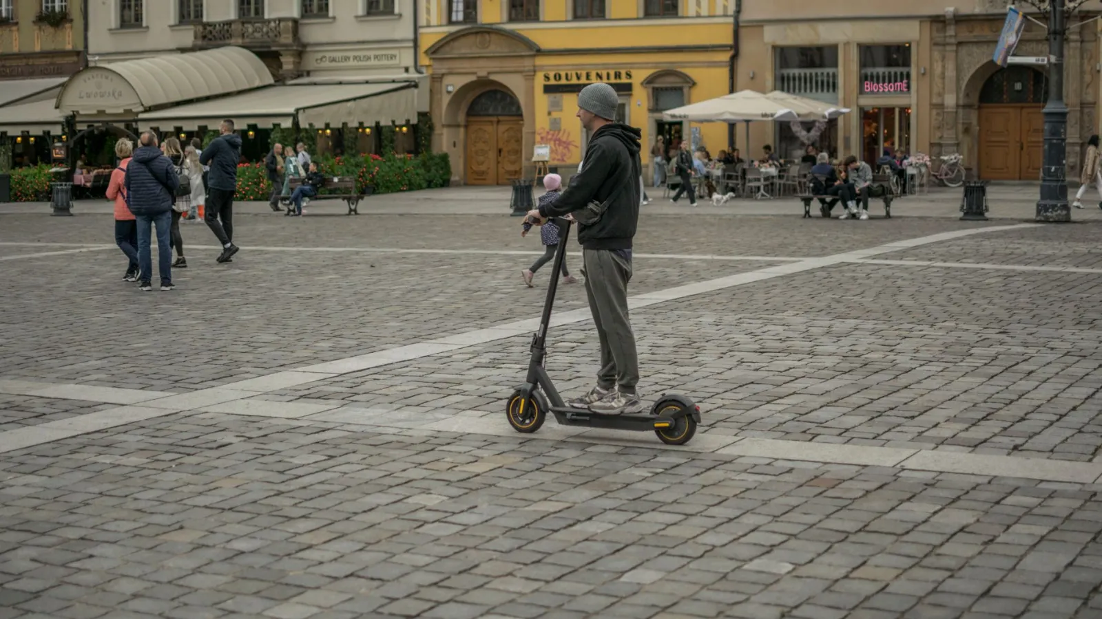 Elektroroller-Fahrer auf einem Platz in Wroclaw, Polen, mit Passanten im Hintergrund.