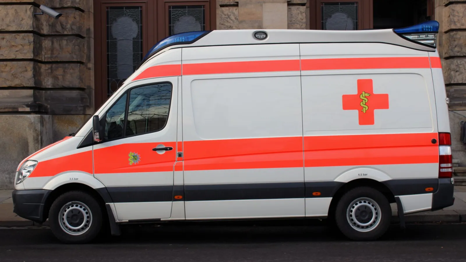 Rotes Kreuz auf weißem Krankenwagen mit orangen Streifen vor einem Gebäude