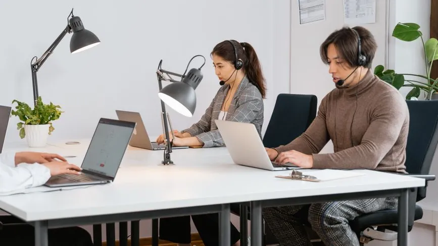 Callcenter-Mitarbeiter mit Headset arbeiten an Laptops in einem modernen Büro.