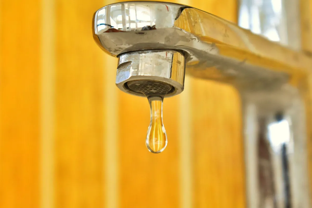 Tropfender Wasserhahn mit Wassertropfen vor gelbem Hintergrund
