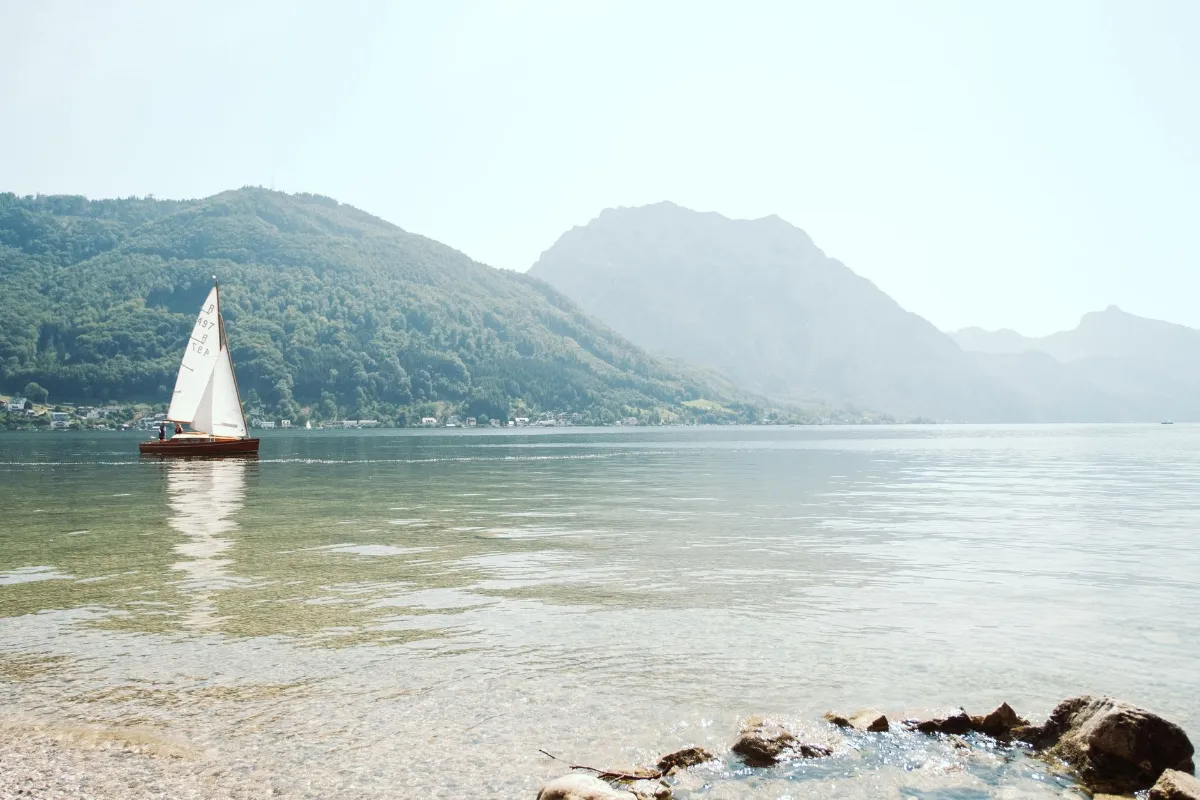 Segelboot mit zwei Personen auf einem Bergsee in Österreich, umgeben von bewaldeten Bergen.
