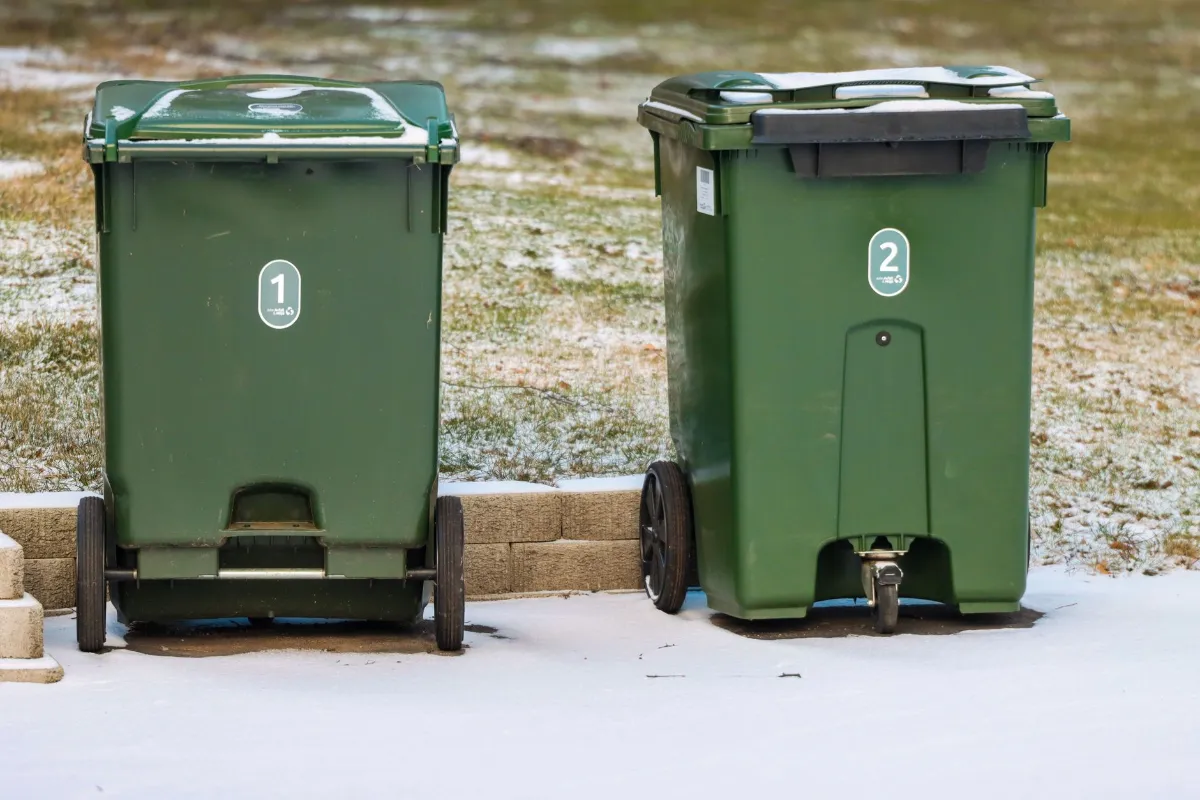 Mülltonnen mit den Nummern 1 und 2 stehen im Schnee vor einer Ziegelmauer.