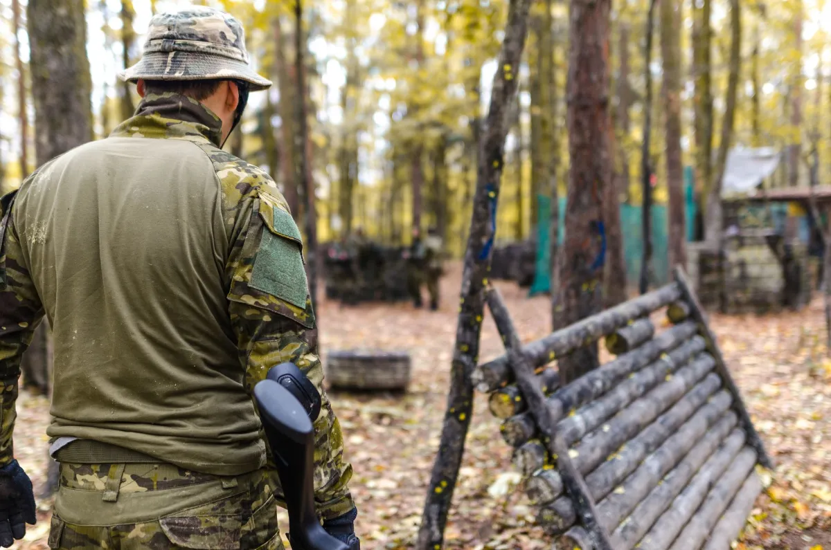 Paintballspieler im Tarnanzug mit Gewehr im Wald auf einem Spielfeld mit Hindernissen
