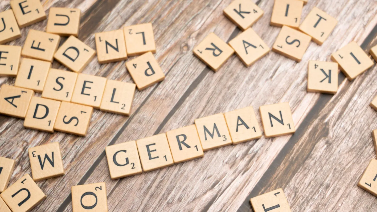 Scrabble-Steine mit den Wörtern „GERMAN“ und „ADSELL“ auf Holzhintergrund