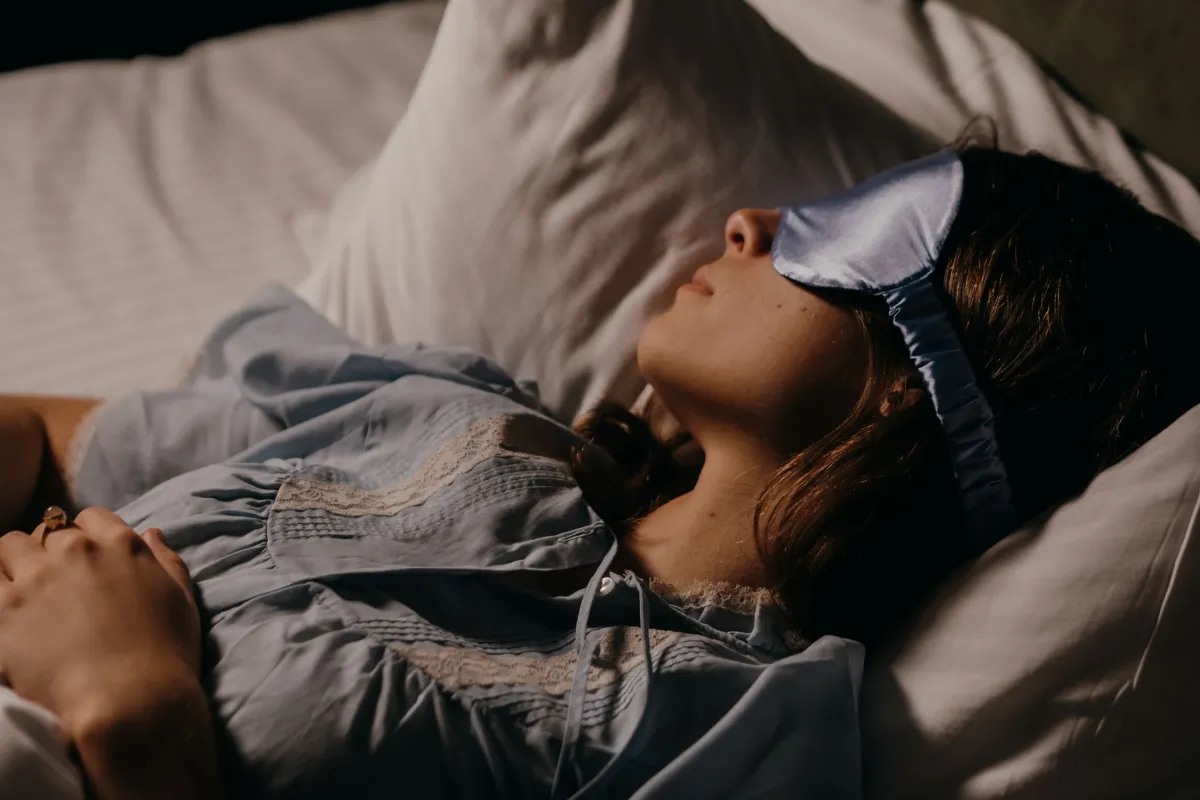 Junge Frau mit Schlafmaske liegt im Bett auf einem Kissen und schläft.