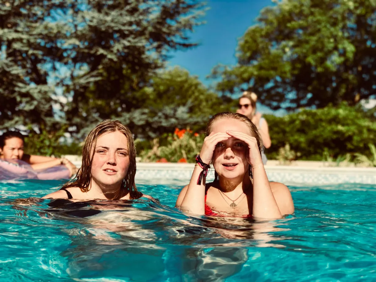 Zwei junge Frauen planschen im Pool an einem sonnigen Tag, im Hintergrund eine weitere Person
