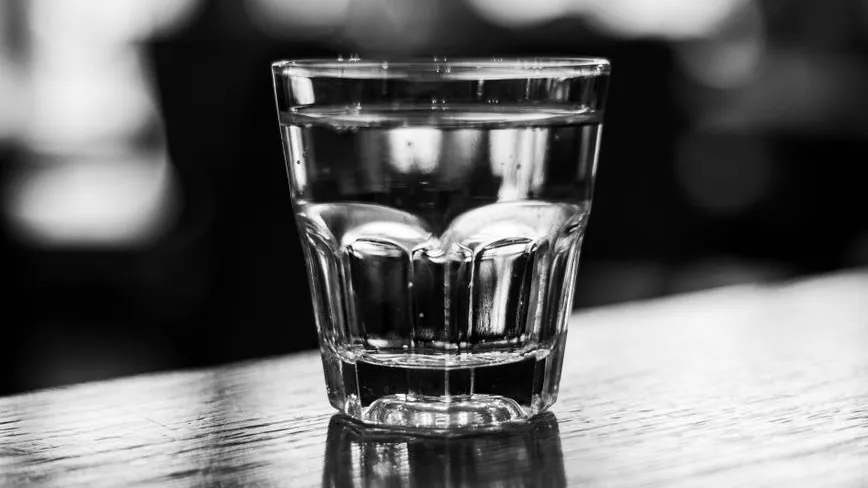 Glas mit Wasser steht auf Holztisch, unscharfer Hintergrund