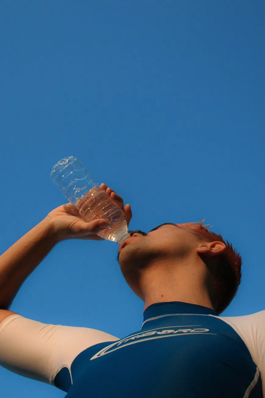 Mann mit gefärbten Haaren trinkt Wasser aus Plastikflasche vor blauem Himmel