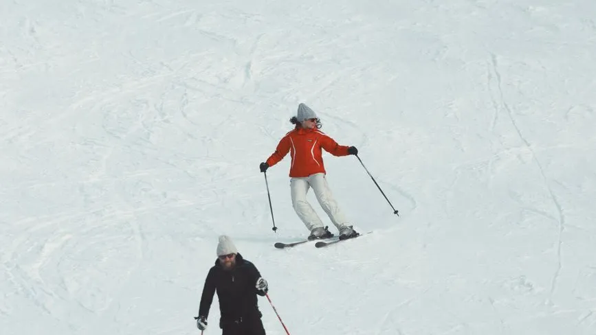 Skifahrer in Orange und Schwarz fahren auf einem verschneiten Hang in den Alpen