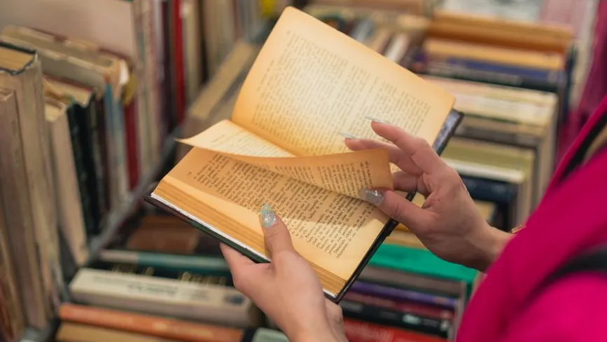 Buchhändlerin blättert in einem antiquarischen Buch vor einem Regal voller alter Bücher.