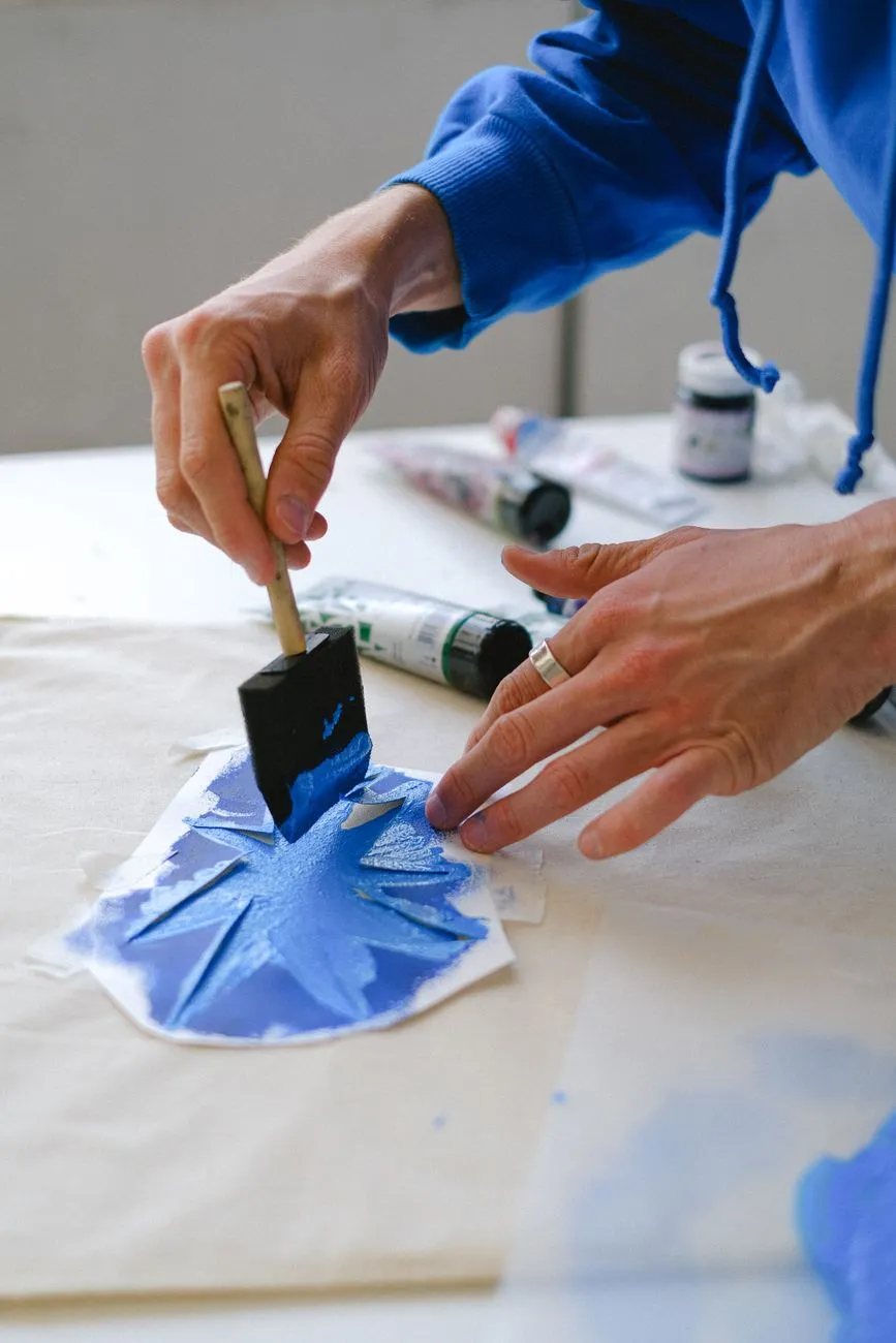 Person mit Schaumstoffpinsel malt Sternschablone auf Stoff mit blauer Farbe