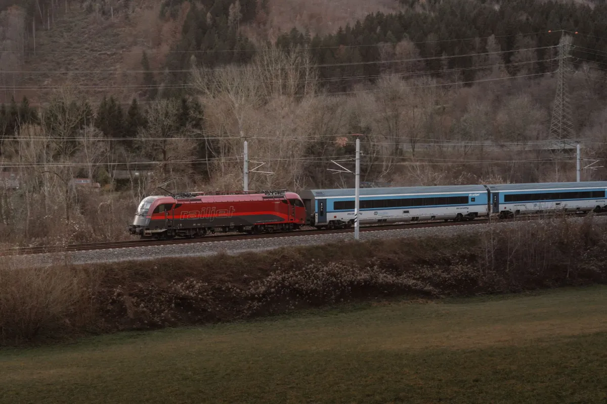 Railjet-Zug fährt durch eine bewaldete Landschaft in Österreich auf der Strecke nach Wien.