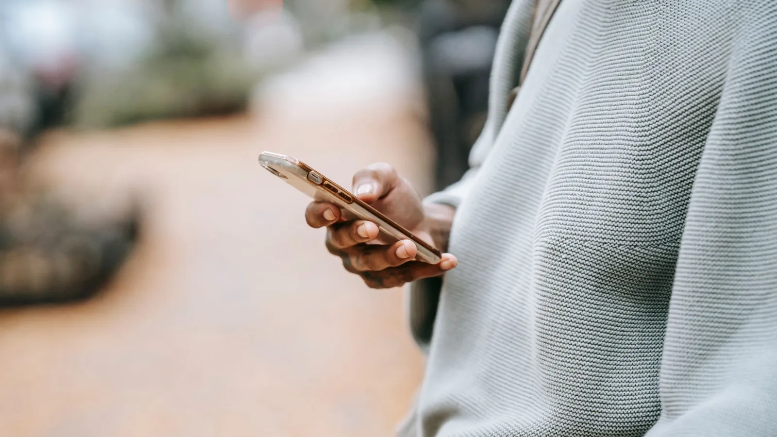 Mann hält Smartphone in der Hand, trägt Strickpullover, unscharfer Hintergrund
