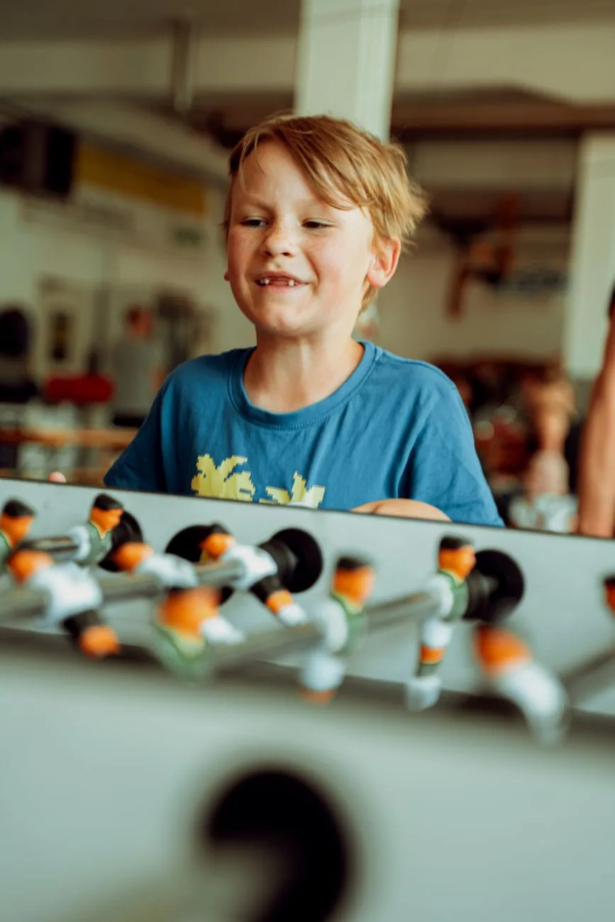 Bub mit Sommersprossen spielt Tischfußball in einem Innenraum