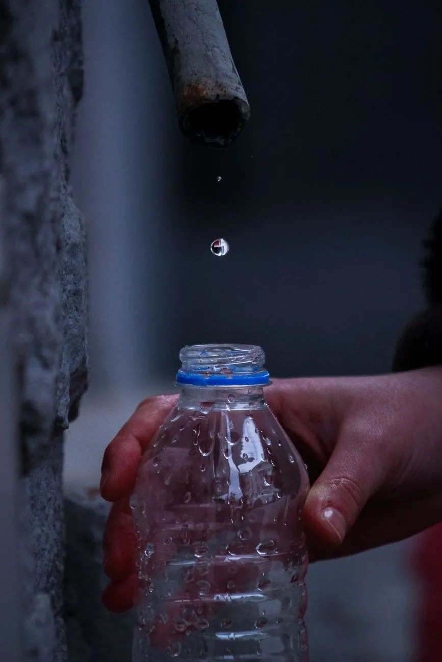Wasser tropft aus altem Rohr in eine Plastikflasche, die eine Hand hält.
