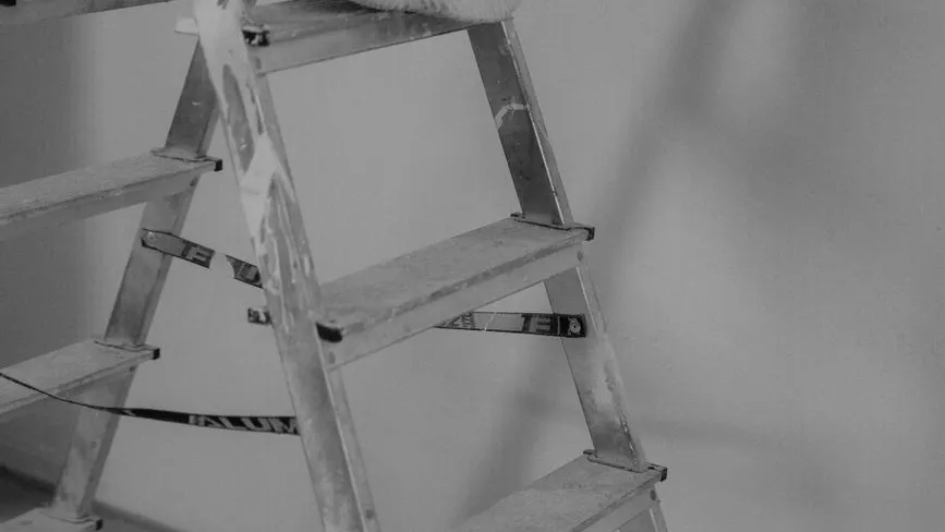 Tragbare Leiter aus Aluminium steht vor einer hellen Wand, Teilansicht