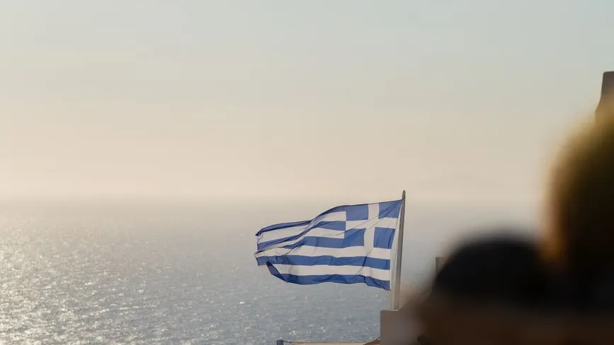 Griechische Flagge weht über dem Meer vor einem hellen Himmel