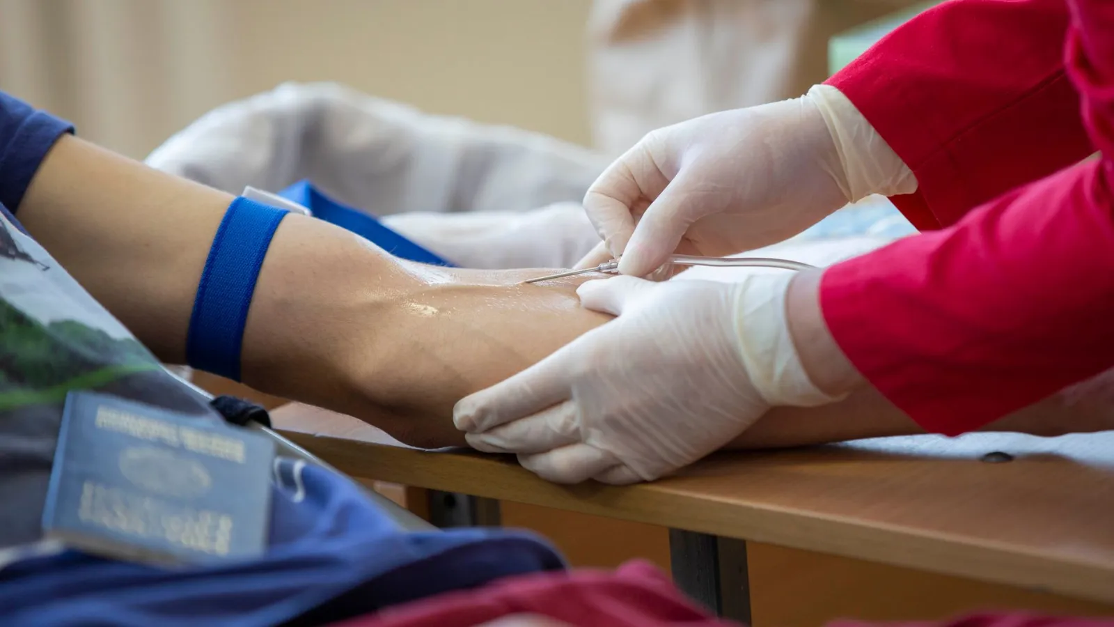 Blutspende: Sanitäterin mit Handschuhen sticht Nadel in Arm eines Spenders