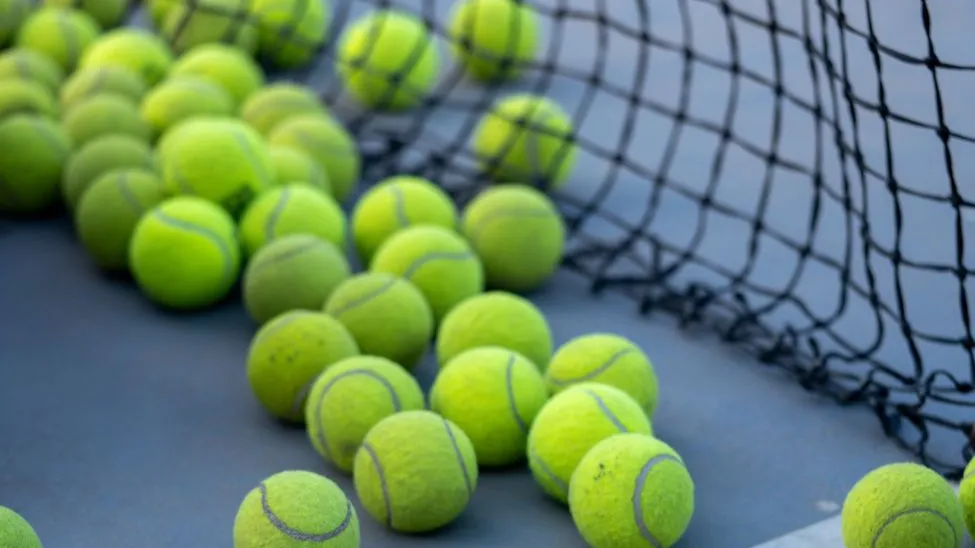 Tennisbälle liegen auf einem blauen Hartplatz neben einem Netz.