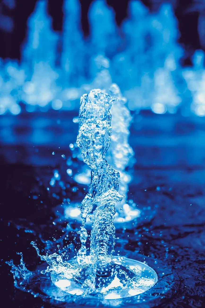 Brunnenwasserstrahl in der Nacht, beleuchtet von blauen Lichtern.