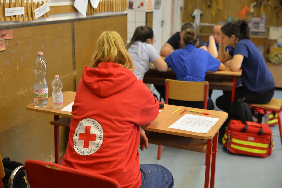 Ungarischer Rotkreuz-Mitarbeiterin in roter Kapuzenjacke sitzt im Klassenzimmer.