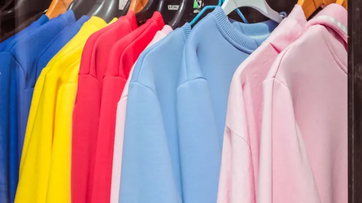 Pullover in bunten Farben hängen auf Kleiderbügeln nebeneinander in einer Reihe.