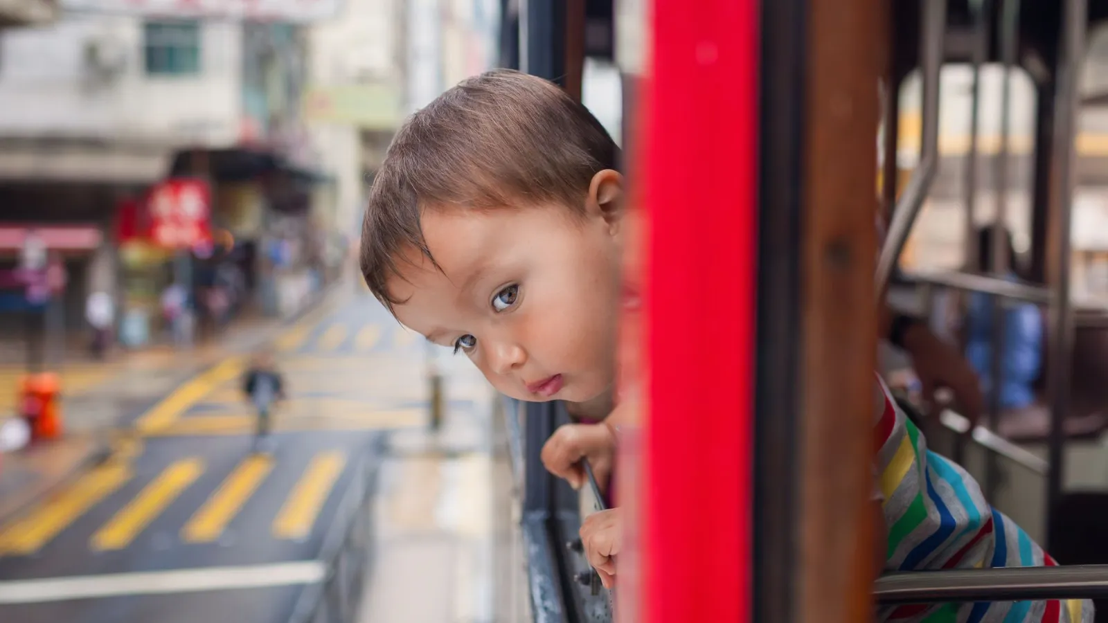 Kleinkind schaut aus der Trambahn in Hongkong auf die Straße