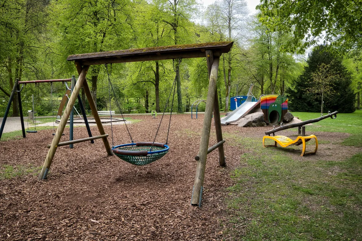 Spielplatz mit Schaukeln, Rutsche und Wippe in einem grünen Park
