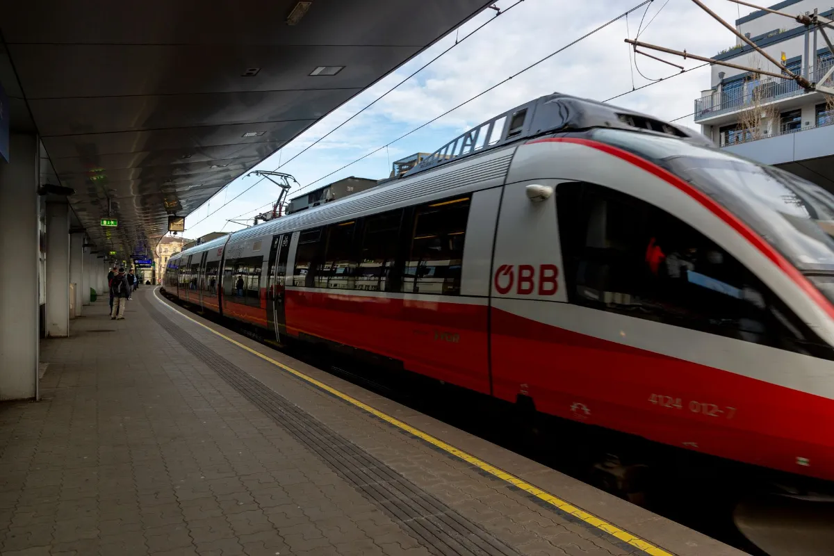 ÖBB Zug fährt in Wien Hauptbahnhof ein, Personen warten am Bahnsteig unter einem Vordach.