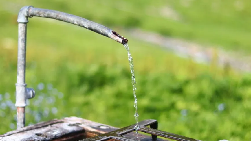 Wasser fließt aus einer Metallleitung in einer grünen Berglandschaft.